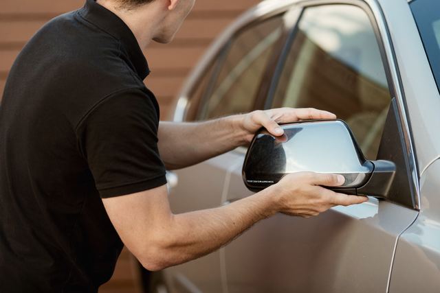 Technician fitting new mirror glass to a car side mirror — replace side mirror glass